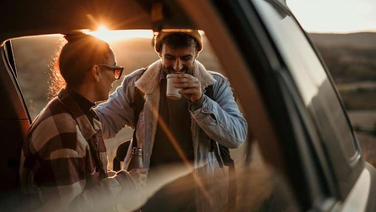man drinking coffee while talking to wife in the car