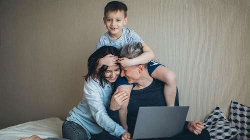 Couple embrace in front of laptop screen online with child on shoulders